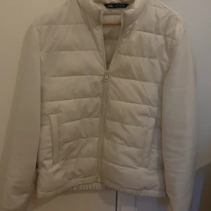 Vit quiltad pufferjacka från Zara Man - Säljer en stilren vit pufferjacka från Zara Man. Jackan har quiltad design, dragkedja framtill och två fickor på sidorna. Perfekt för kyligare dagar men funkar även på lite varmare dagar, enkel att matcha med olika outfits. Storlek S. Kan skickas samma dag som köpet
