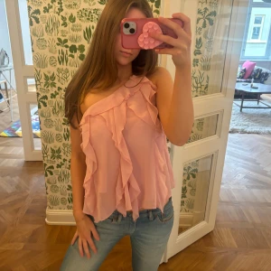 Ljusrosa volang topp från Zara - Säljer en ljusrosa volangtopp från Zara, one shoulder-modell. Aldrig använd och prislappen sitter fortfarande kvar!!💕💕