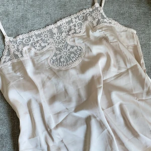 Ljusrosa linnetopp med spets - Säljer en ljusrosa linnetopp med tunna axelband och vacker spetsdetalj upptill. Toppen har en lös passform och är perfekt för varma dagar eller som lager under en kofta.