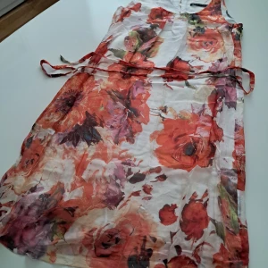 Blommig långklänning från Expresso - Säljer en somrig långklänning från Expresso med färgstarkt blommönster i rött, orange och lila toner. Klänningen är ärmlös, har ett knytband i midjan och är tillverkad i 100% Siden för en luftig känsla och foder i Viscose. 