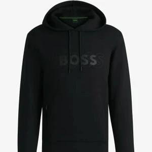 Svart hoodie från BOSS - Säljer en svart hoodie från BOSS med diskret logga på bröstet. Tröjan har huva med dragsko och en stor magficka framtill. Perfekt för en avslappnad och stilren look.