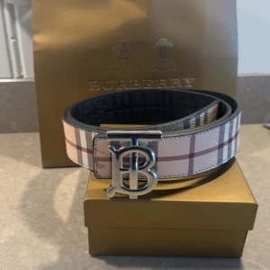  Bur$erry bälte  - Säljer ett klassiskt bälte från Bur$erry med deras ikoniska rutig mönster i beige, svart och rött. Bältet har ett stort silverfärgat spänne med Burberrys logotyp. Perfekt accessoar för att lyfta din outfit. Mer bilder och mer information kring produkten via intresse