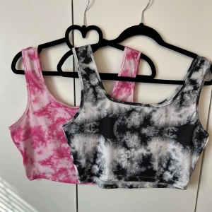 Två tie-dye linnetoppar i rosa och svart - Säljer två trendiga linnetoppar i tie-dye mönster, en i rosa och vit och en i svart och vit. Båda har breda axelband och ärmlös design, perfekta för sommaren eller träning.