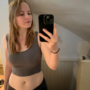 Grå ribbad linnetopp från Stradivarius - Säljer en grå ribbad linnetopp från Stradivarius. Toppen har en croppad passform och breda axelband. Perfekt att matcha med jeans eller kjol för en enkel och stilren look.