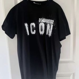 Svart t-shirt från Dsquared2 med tryck - Svart t-shirt från Dsquared2 med stort vitt tryck på bröstet där det står 'ICON'. Klassisk rund hals och korta ärmar. Perfekt för dig som gillar streetwear och vill sticka ut med en ikonisk look.