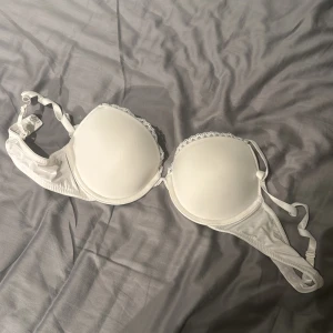 Vit bh från H&M - Säljer en vit bh från H&M med lätt vadderade kupor och spetsdetalj längs kanten. Justerbara axelband och klassisk knäppning bak. Perfekt basplagg i garderoben.
