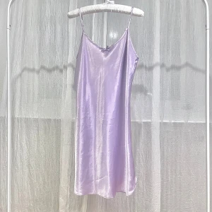 Lila satinklänning - Elegant lila klänning i satin med smala axelband och v-ringad hals. Klänningen har en slät och glansig yta som ger en lyxig känsla. Passar även som en nattlinne. För storlek M-L.