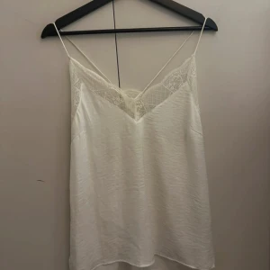 Vitt satinlinne från Vila - En luftig satin topp med spets detaljer. Passar både till jeans och kjol och är i storlek 36!
