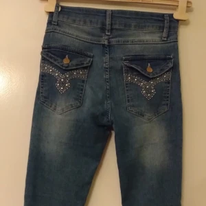 Blå jeans med broderade bakfickor - Säljer ett par väldigt snygga blåa utsvängda jeans med broderade detaljer på bakfickorna💙🤩. Xs men känns lite mer som S.