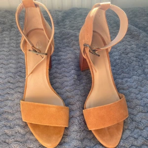 Bruna mockasandaler från Rizzo - Snygga bruna sandaler i mocka från Rizzo med en elegant klack och justerbart spänne runt ankeln. Perfekta för sommarens alla tillfällen. Den öppna designen ger en luftig känsla och den mjuka mockan ger en lyxig touch. HELT oanvända, säljer då dom ej passade mig. Storlek 39. Nypris 1300 säljer för 850 i sin kartong, fint märke. 