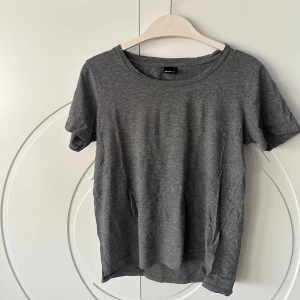 Grå t-shirt från Gina Tricot - Säljer en enkel och stilren grå t-shirt från Gina Tricot. Perfekt basplagg med rund hals och korta ärmar. Gjord i mjukt material för en bekväm känsla. Passar till alla tillfällen!