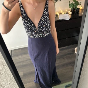 Mörkblå långklänning med paljetter - Elegant mörkblå långklänning med glittrig paljettöverdel och djup v-ringning. Klänningen har en slits framtill och en öppen rygg som ger en sofistikerad look. Perfekt för festliga tillfällen. Jag är 160 lång och klänningen går ner till marken när jag har på mig klackar som är ca 6cm höga! Klänningen är insydd men går att få större i midja men inte att förlänga tyvärr!💕💕skriv för mer frågor!