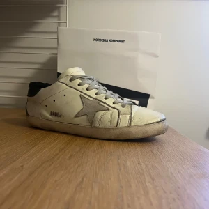 Golden goose sneakers - Snygga vita sneakers från Golden Goose med en grå stjärna på sidan och svarta detaljer vid hälen. Skorna har en klassisk snörning och en bekväm sula. Perfekta för en stilren och avslappnad look. De är använda men fortfarande i ett bra skick!
