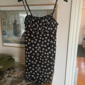 Svart blommig klänning från Bershka - Säljer en svart klänning med vita blommor från Bershka. Klänningen har smala axelband och en figurnära passform. Perfekt för sommarens varma dagar!