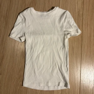 Vit t-shirt - Säljer en stilren vit ribbad t-shirt med korta ärmar. Perfekt basplagg för alla tillfällen. Skön och enkel att matcha med olika outfits.