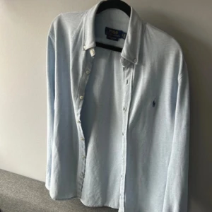 Ljusblå skjorta från Polo Ralph Lauren - Snygg ljusblå skjorta från Polo Ralph Lauren med klassisk krage och knappar framtill. Skjortan har en broderad logotyp på bröstet och är perfekt för en stilren look.