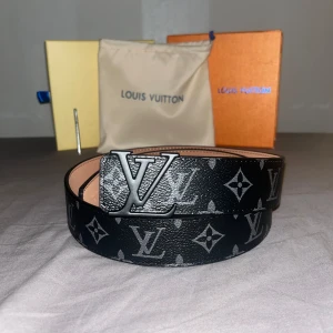 Svart bälte från Louis Vuitton - Snyggt svart bälte från Louis Vuitton med det ikoniska LV-mönstret och ett stilrent LV-spänne i silver. Perfekt för att ge din outfit en lyxig touch.