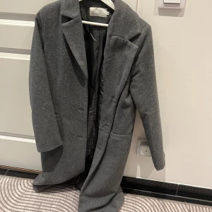 Grå kappa från NLY Trend - Snygg grå kappa från NLY Trend i storlek 34. Den har en klassisk design med långa ärmar och en stilren look. Perfekt för kyligare dagar.