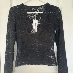 Svart spetsblus från Gina Tricot - Elegant svart spetsblus från Gina Tricot med v-ringning och långa ärmar. Perfekt för en stilfull outfit. Blusen har en figurnära passform och är idealisk för både vardag och fest. Säljer toppen eftersom jag inte fått användning av den☺️