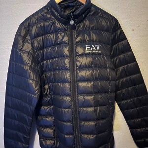 Svart pufferjacka från Emporio Armani - Snygg svart pufferjacka från Emporio Armani med dragkedja framtill. Köpt förra året från zalando för ca 2000kr. Använd 1 Gång så Otroligt fräsch