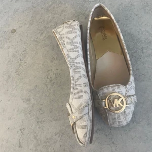 Student skor, ballerina skor  Michael Kors - Snygga beige loafers från Michael Kors med ett diskret mönster och en stor guldfärgad MK-logga på ovansidan. Skorna har en klassisk loaferdesign med rundad tå och är perfekta för en stilren look. Ord pris 2000 kr
