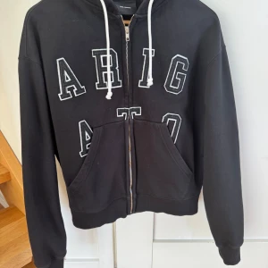 Svart hoodie från Axel Arigato - Säljer en svart hoodie från Axel Arigato med vit text på framsidan. Den har en dragkedja och justerbar huva med vita snören. En tröja som är lite oversized i modellen. Väldigt bra skick. Storlek:XS. Nypris:2300kr. Säljer för:1000