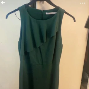 Grön klänning med volangdetalj från Zara  - Elegant grön klänning med volangdetalj framtill. Perfekt för en stilren look.