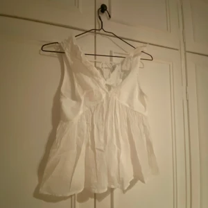 Vit topp från Gina Tricot - Säljer en söt vit topp från Gina Tricot. Toppen har volangdetaljer vid axlarna och en v-ringad design. Perfekt för varma dagar och kan enkelt matchas med olika outfits. 🕊️