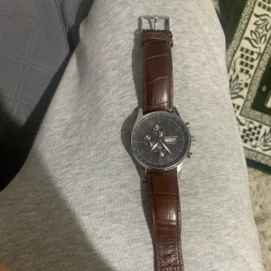 Jacques Lemans klocka med brun läderrem - Snygg Jacques Lemans klocka med brun läderrem och grå urtavla. Klockan har kronograf och är vattentät upp till 10 ATM. Den har en stilren design med silverfärgade detaljer och tydliga markeringar.