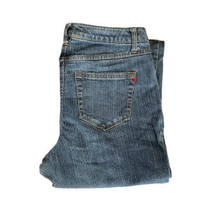 Blå jeans med hjärtdetalj - Snygga blå jeans med en liten röd hjärtdetalj på bakfickan. De har en klassisk femficksdesign och en rak passform som ger en tidlös look. Perfekta för en avslappnad stil.