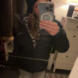 Svart pufferjacka från Peak Performance - Säljer en svart pufferjacka från Peak Performance med huva och diskret logga på bröstet och ärmen. Jackan är vadderad och har en klassisk pufferlook som håller dig varm under kalla dagar. Perfekt för dig som vill ha en stilren och sportig vinterjacka.