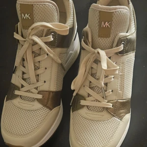 Michael Kors Beige och guld sneakers  - Helt nya Snygga sneakers från Michael Kors i beige och guld som jag fick i julklapp. Dom är små i storleken.Skorna har snörning och en stilren design med meshdetaljer för extra andningsförmåga. Perfekta för en trendig look.