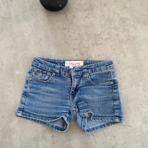 Blå jeansshorts från Vigoss - Snygga blå jeansshorts från Vigoss med coola detaljer på bakfickorna. Perfekta för sommardagar med en avslappnad stil. Shortsen har en klassisk femficksdesign och knappar framtill. Storleken står inte, men rätt så små i storleken så skulle gissa på kanske XXS-XS