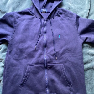 Mörkblå hoodie från Polo Ralph Lauren - Säljer en snygg mörkblå hoodie från Polo Ralph Lauren med dragkedja och klassisk logga på bröstet. Storlek M/S men sitter lite stort i midjan. Kan behövas torktummlas för bättre passform. Endast använd en gång. Pris kan diskuteras vid snabb affär!