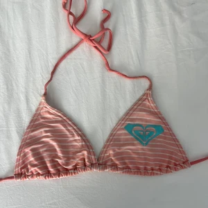 Rosa randig bikini från Roxy - Snygg rosa bikini från Roxy med vita ränder och ett turkost hjärta på toppen. Bikinin har knytband för en justerbar passform. Passar mig som har storlek s-sx men den är justerbar så passar många. Nypris 550kr