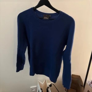 Blå tröja i 100% ull från Oscar Jacobson  - Säljer en stilren blå tröja från Oscar Jacobson i 100% ull. Tröjan har en klassisk rund hals och långa ärmar, perfekt för kyligare dagar. Den är mjuk och bekväm, vilket gör den till ett utmärkt val för både vardag och mer uppklädda tillfällen.