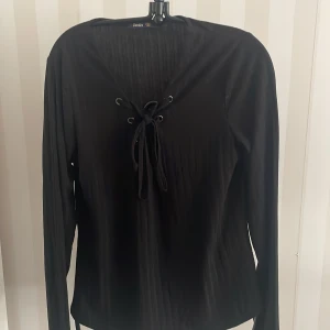 Svart långärmad topp från Crocker - Säljer en stilren svart långärmad topp från Crocker med snörning framtill. Toppen har en ribbad struktur som ger en snygg detalj. Perfekt för en chic look!