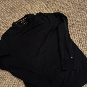Mörkblå tröja från Tommy Hilfiger - Tja tja! Säljer en läskigt snygg mörkblå tröja från Tommy Hilfiger.                      Tröjan är tillverkad i superskön lyxig ull och har långa ärmar med ett snyggt märke nere vid handleden. Tyvärr har den blivit för liten för mig så därför säljer jag den - mvh Edvin