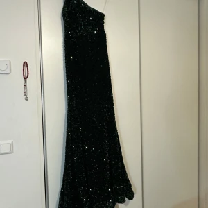 Grön paljettklänning - Snygg grön klänning med paljetter och en axelbandslös design. Perfekt för en festlig kväll med sin glittriga yta och eleganta stil. Klänningen har en lång längd och en smickrande passform.