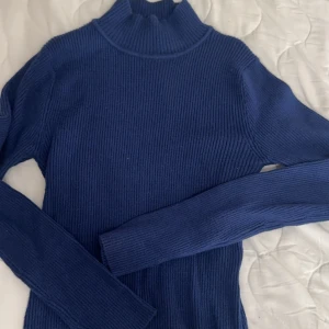 Blå ribbad polotröja - Snygg blå ribbad polotröja med långa ärmar. Perfekt för kyligare dagar och ger en stilren look. Passar bra till både jeans och kjol.