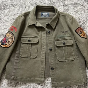 Olivgrön jeansjacka från Crocker - Säljer en olivgrön jeansjacka från Crocker med skitcoola detaljer på ärmarna. Jackan har två bröstfickor med knappar och en klassisk krage. 