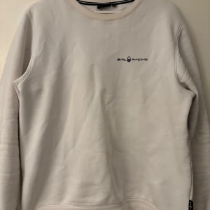 Vit tröja från Sail Racing - Säljer en stilren vit tröja från Sail Racing med rund halsringning och långärmad design. Tröjan har en diskret logotyp på bröstet och en liten detalj på ryggen. Perfekt för en avslappnad och sportig look. Passar även för de som har M. Nypris: 1.100