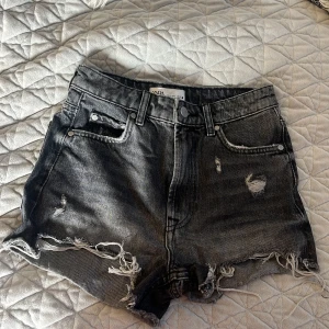 Svarta jeansshorts från Zara - Snygga svarta jeansshorts från Zara med slitna detaljer och fransar. Perfekta för en avslappnad stil. De har en klassisk femficksdesign och knappgylf.