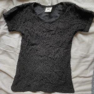 Svart kortärmad topp  - Snygg, tight svart topp med korta ärmar och ett intressant texturerat mönster. Perfekt att styla med. Köpt på stadsmissionen. Passar storlek S-XS