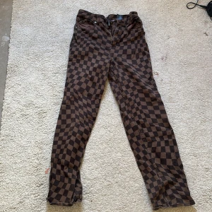 Bruna rutiga byxor - Snygga bruna byxor med ett coolt rutigt mönster. De har en dragkedja fram och är perfekta för en unik stil. Passar bra till både vardag och speciella tillfällen.