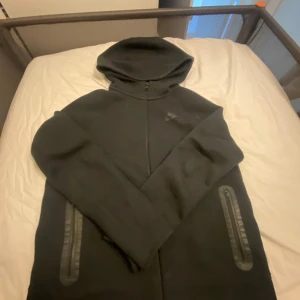 Svart huvtröja från Nike - Säljer en svart huvtröja från Nike med dragkedja och huva. Tröjan har långa ärmar och två fickor med dragkedja framtill. Perfekt för en casual look eller träning.säljs på grund av att den är för liten (Nike tech new gen)den passar om man är ungefär 158-160 xl i barnstorlek 