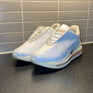 Nike Air Max 720 sneakers VITA - Snygga vita Nike Air Max 720 sneakers med en futuristisk design och synlig luftenhet i sulan. Skorna har en diskret Nike-logga på sidan och snörning framtill. Perfekta för en stilren look. Otroligt sällsynta med subtila oranga detaljer. Väldigt fint skick.