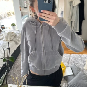 Grå hoodie från Juicy Couture - Säljer en mjuk och stilren grå hoodie från Juicy Couture. Den har en dragkedja framtill och en praktisk huva med knytband. Perfekt för en avslappnad look.