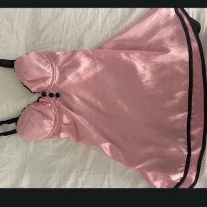 Rosa vintage nattklänning  - Charmig rosa vintage natt klänning med svarta axelband och knappar. Klänningen har en söt rosett bak som man knyter och svarta kanter som ger en fin kontrast. Perfekt för en speciell kväll! Storlek M men passar S/XS 😊