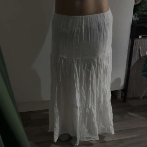 Vit långkjol från Gina Tricot - Säljer en vit långkjol från Gina Tricot. Kjolen har en luftig och avslappnad passform med ett lätt rynkat tyg som ger en fin struktur. Perfekt för varma dagar när du vill känna dig både bekväm och stilren.